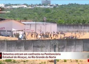 19/01/2017 10h34 - Atualizado em 19/01/2017 14h21 Presos de Alcaçuz entram em confronto; há mortos e feridos, diz PM Conflito aconteceu após detentos voltarem a ocupar os telhados. Penitenciária, a maior do RN, foi palco de matança no fim de semana. Do G1 RN FACEBOOK Presos da Penitenciária Estadual de Alcaçuz, maior presídio do Rio Grande do Norte, entraram em confronto na manhã desta quinta-feira (19). Após subirem em telhados dos pavilhões, membros de duas facções se enfrentaram. Pedras, barras de ferro e vigas de madeira são arremessadas de um lado a outro. Há mortos e feridos, segundo a PM --uma ambulância socorreu um detento baleado. A Polícia Militar está na área externa da unidade. Do alto das guaritas, policiais fizeram disparos na tentativa de conter a confusão. Confronto entre presos em Alcaçuz (Foto: Reprodução/TV Globo) Confronto entre presos em Alcaçuz (Foto: Reprodução/TV Globo) O repórter Ítalo Di Lucena, da Inter TV Cabugi, está na área externa de Alcaçuz. Ele informa que há fumaça na parte interna, barulhos de tiros e de quebra-quebra no local. Por volta das 11h30 (horário de Brasília) o helicóptero Potiguar I, da secretaria de Segurança Pública do estado, chegou ao local para auxiliar na operação. Durante o confronto, os presos abandonaram as barricadas que haviam montado para se proteger e foram em direção à facção rival, atirando objetos. Foi possível ver detentos aparentemente feridos sendo transportados em carrinhos de carga. Por volta das 13h (horário de Brasília), a situação estava mais calma. Os grupos em confronto haviam voltado para as barricadas e telhados dos pavilhões, mas ainda lançavam objetos um contra o outro e trocavam ameaças. A polícia permanecia na área externa do presídio, onde parentes dos presos buscavam informações. A dona de casa Jéssica de Oliveira, de 26 anos, afirma que o marido lhe contou, pelo telefone, ter sido ferido na perna. "O Estado não pode deixar todo mundo assistir a nossos maridos morrerem desse jeito", disse. Na quarta-feira (18), 220 membros da facção criminosa Sindicato do RN foram retirados de Alcaçuz, para evitar o confronto com presos do Primeiro Comando da Capital (PCC) que estão no presídio. Ainda há, entretanto, membros do Sindicato no local, além de detentos que não são ligados a nenhuma facção. No total, há cerca de 1,2 mil detentos em Alcaçuz, quase o dobro da capacidade. No último fim de semana, presos do PCC invadiram a área onde ficam os integrantes do Sindicato do RN. No confronto, 26 detentos morreram. Desde a última terça-feira (17), a prisão se tornou um verdadeiro cenário de guerra
